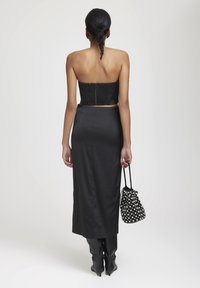 Haut noir sans bretelles en tissu texturé, associé à une jupe noire en satin élégante. Les accessoires comprennent un sac à main perlé noir et blanc.