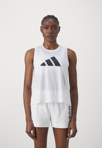Biela bezrukávová športová košeľa s čiernym logom Adidas, s voľným strihom a mäkkou textúrou, v kombinácii s bielymi šortkami s čiernym brandingom.
