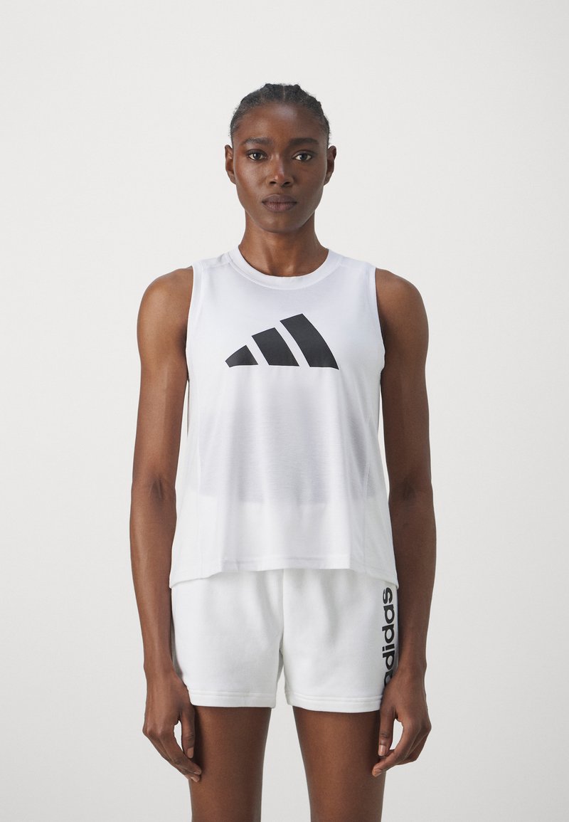 Biela bezrukávová športová košeľa s čiernym logom Adidas, s voľným strihom a mäkkou textúrou, v kombinácii s bielymi šortkami s čiernym brandingom.