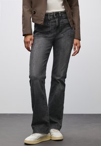Jeans in denim nero con una vestibilità dritta, cinque tasche, leggera scoloritura e cuciture a contrasto, abbinati a sneakers bianche.