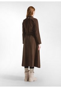 Vestito marrone a maniche lunghe con vita aderente, texture liscia e colletto. Indossato sopra stivali beige e calze a coste.