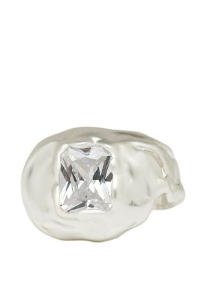 Bague en argent avec un anneau irrégulier et ondulé présentant une grande pierre précieuse rectangulaire transparente au centre sur fond blanc.