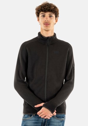 Chaqueta negra con cremallera y cuello alto, hecha de tejido elástico. Cuenta con bolsillos laterales, mangas largas y puños con orificios para los pulgares.