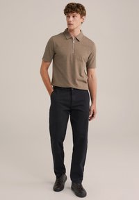 Tricou polo tricotat de culoare maro, cu guler cu fermoar, asociat cu pantaloni drepti de culoare bleumarin închis și adidași negri. Textură netedă, croială casual.