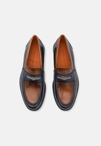 Mocassins en cuir marine et marron avec une sangle texturée, des coutures contrastantes et un design épuré. Fini lisse avec un léger éclat.