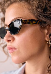 Kacēnu formas saulesbrilles ar brūna bruņurupuča rakstu, tumšiem stikliem un biezām acetāta rāmīšiem. Metāla uzlabojumi pie kājiņām piešķir detaļas.