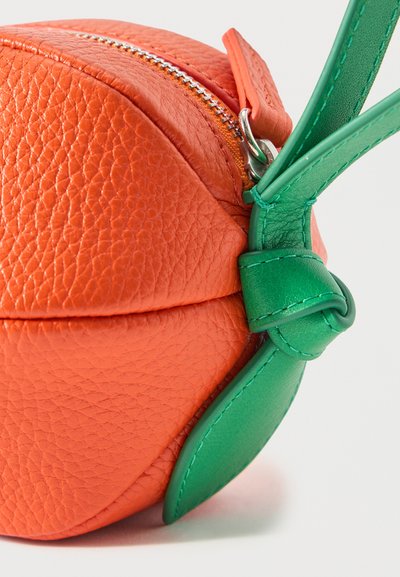 Sac rond en cuir orange texturé avec une fermeture éclair argentée et une sangle en cuir verte attachée, en forme de feuille.