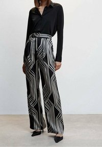 Black long-sleeve shirt paired with high-waisted, wide-leg trousers featuring a bold black and white geometric pattern. Points: sleek fabric, belt.