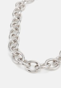 Stříbrný náhrdelník s řetězem zdobeným velkými, hladkými kulatými články s leštěným povrchem, odrážející světlo na jednobarevném bílém pozadí.