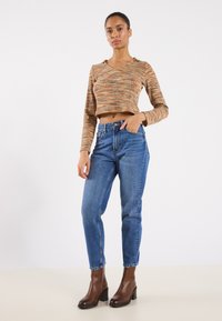 Top crop a righe marroni e arancioni con maniche lunghe, abbinato a jeans blu a gamba dritta e stivaletti con tacco marroni.
