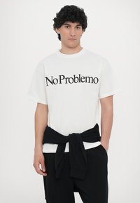 White short-sleeve t-shirt with "No Problemo" printed in black text. Black waistband tied around the waist over black pants.