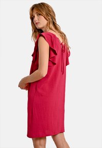 Abito fucsia con maniche corte a volant, vestibilità comoda e chiusura a legatura sul retro, realizzato in tessuto testurizzato.