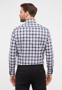 Camicia a maniche lunghe da uomo in tela a quadri navy e bianco. Presenta un colletto e polsini con bottoni. Il tessuto appare liscio con una vestibilità strutturata.