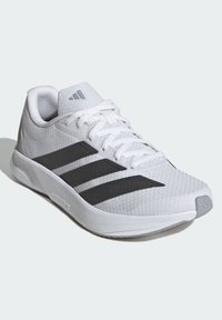 Weißer Sportschuh mit einem texturierten Mesh-Obermaterial, ausgestattet mit schwarzen Streifen und einer verstärkten Zehenkappe. Leichtes Design mit flacher Sohle.