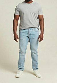 Jeans de color azul claro y una camiseta gris de manga corta. Los jeans tienen un corte clásico y el conjunto se complementa con zapatillas blancas.