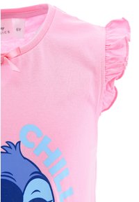 Camicia corta rosa in cotone con accenti a volant, un personaggio dei cartoni animati blu navy e un testo azzurro che dice "CHILL".