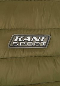 Olivgrön puffjacka med quiltat mönster, med en svart och silver "KANI SPORT" logotyp patch som är tydligt synlig.