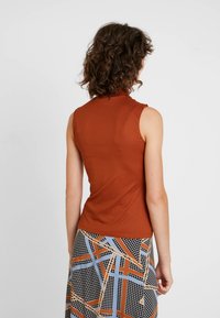 Top de canalé sin mangas en naranja quemado, con cuello alto. Combinado con una falda estampada multicolor con líneas geométricas.