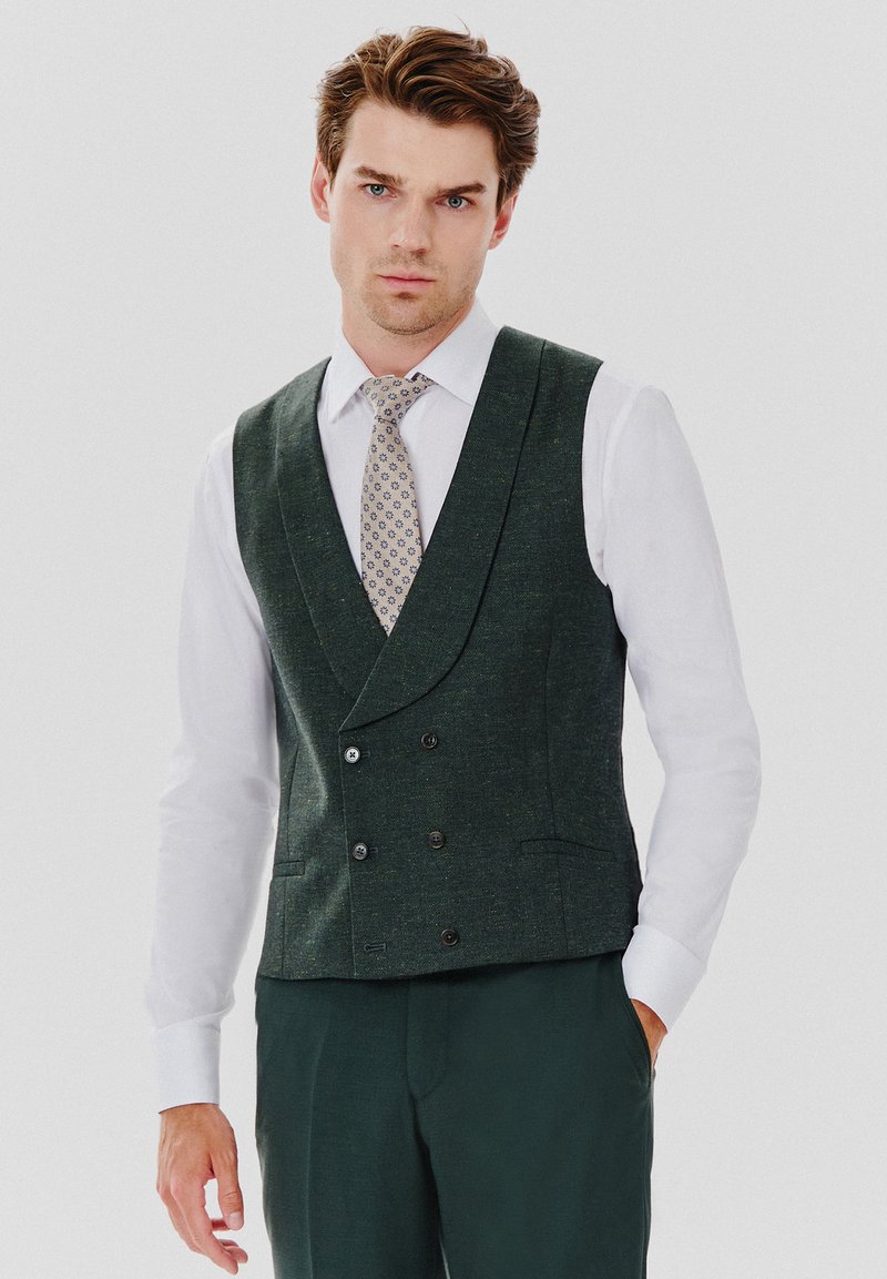 Zielona kamizelka dwurzędowa z teksturowanej tkaniny, z dwoma bocznymi kieszeniami, w połączeniu z białą koszulą i wzorzystym krawatem.