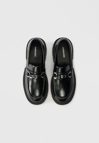 Black leather slip-on shoes with a rounded toe, decorative silver hardware, and a chunky black sole. Smooth texture with a polished finish.
