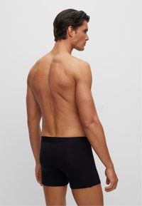 Schwarze Baumwoll-Boxershorts mit glatter Textur, elastischem Bund und passgenauer Form, vor einem neutralen Hintergrund.