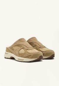 Brune ruskind slip-on-sko med en tekstureret finish, polstrede indersåler og en hvid gummisål, der har diskrete designlinjer og ingen synlige metaldele.