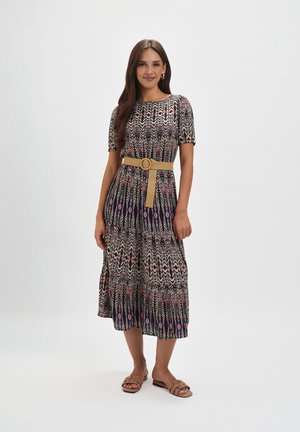 Maxi sukienka z czarno-biało-czerwonym wzorem, krótkimi rękawami, dopasowaną talią z beżowym paskiem oraz płaskimi sandałami.