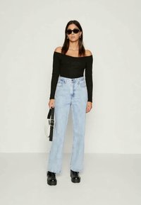 Μαύρη μπλούζα με ανοιχτούς ώμους και μακριά μανίκια, ανοιχτό μπλε τζιν ψηλόμεσο με φαρδιά γραμμή, χοντρές μαύρες πλατφόρμες και μια μαύρη τσάντα ώμου με ασημί λεπτομέρειες.