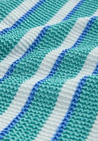 Tekstureeritud kangas, kus on vahelduvad lainelised triibud rohelises, türkiissinis ja valges. Triipude vahel sinised aktsendid lisavad sügavust ja mustrit.