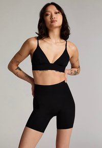 Svart sømløs bralette med V-utringning og tynne stropper, kombinert med høytlivs sorte shorts. Glatt tekstur med en tettsittende design.