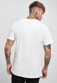 T-shirt bianco in cotone con maniche corte, scollo a giro e vestibilità rilassata. Presenta una texture liscia e un orlo leggermente arrotondato sul retro.