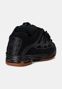 Scarpa sportiva nera con tomaia testurizzata, design a onde distintive, dettagli utilitari e suola in gomma per una maggiore aderenza.