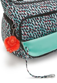 Multicolored backpack featuring a pattern of small shapes in red and black on a light blue background. Includes an orange fuzzy monkey keychain.