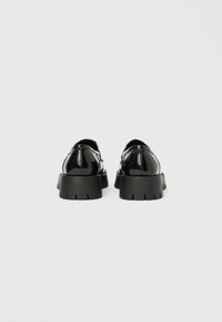 Čierne topánky z lakovanej kože s okrúhlou špičkou, hrubou podrážkou s dezénom a hladkým povrchom, vyznačujúce sa minimálnym šitím a elegantným dizajnom.