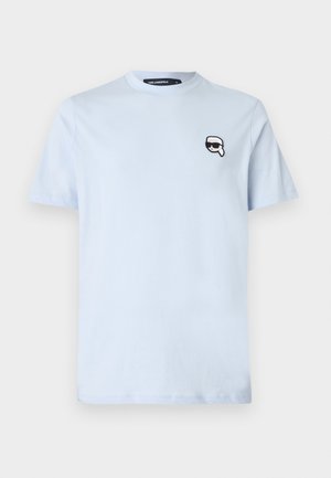 Lyseblå bomull T-skjorte med korte ermer, rund hals og et lite svart-hvitt grafisk bilde av et ansikt med solbriller på venstre bryst.