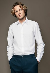 White button-up shirt with a pointed collar, long sleeves, and a textured finish, paired with dark blue trousers featuring a front button closure.