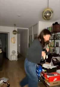 Žena v obývacím pokoji drží boty, obklopena několika krabicemi na tenisky a policemi s knihami a dekoracemi.