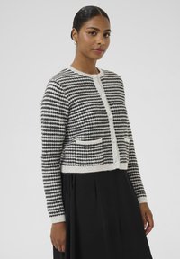 Cárdigan a rayas en blanco y negro hecho de material suave, con botones redondos, dos bolsillos frontales y un diseño corto.