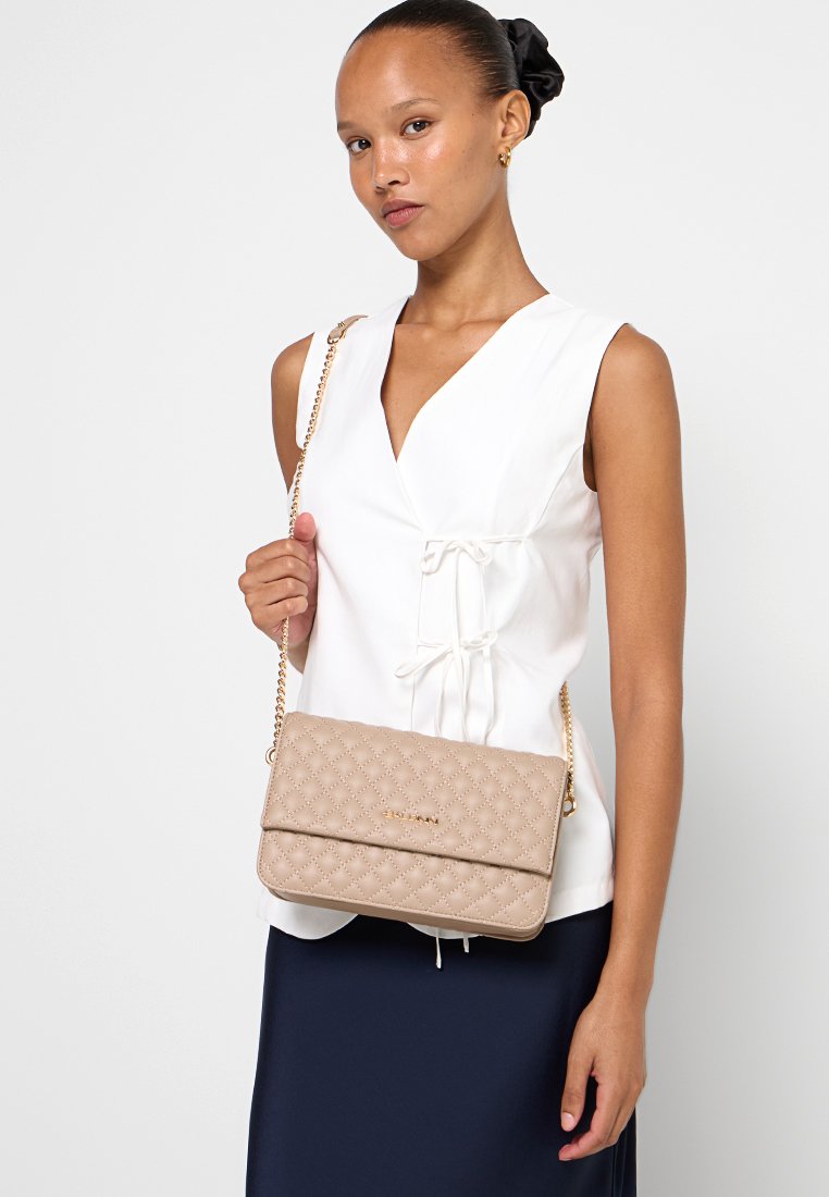 Beige gesteppte Umhängetasche mit einer Kettenriemen, ausgestattet mit einem gefalteten Klappdeckel, goldfarbenen Beschlägen und einem strukturierten Muster.