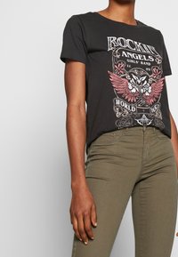 Czarny bawełniany t-shirt z grafiką w czerwone i białe detale, z krótkimi rękawami i okrągłym dekoltem, w połączeniu z oliwkowymi spodniami.