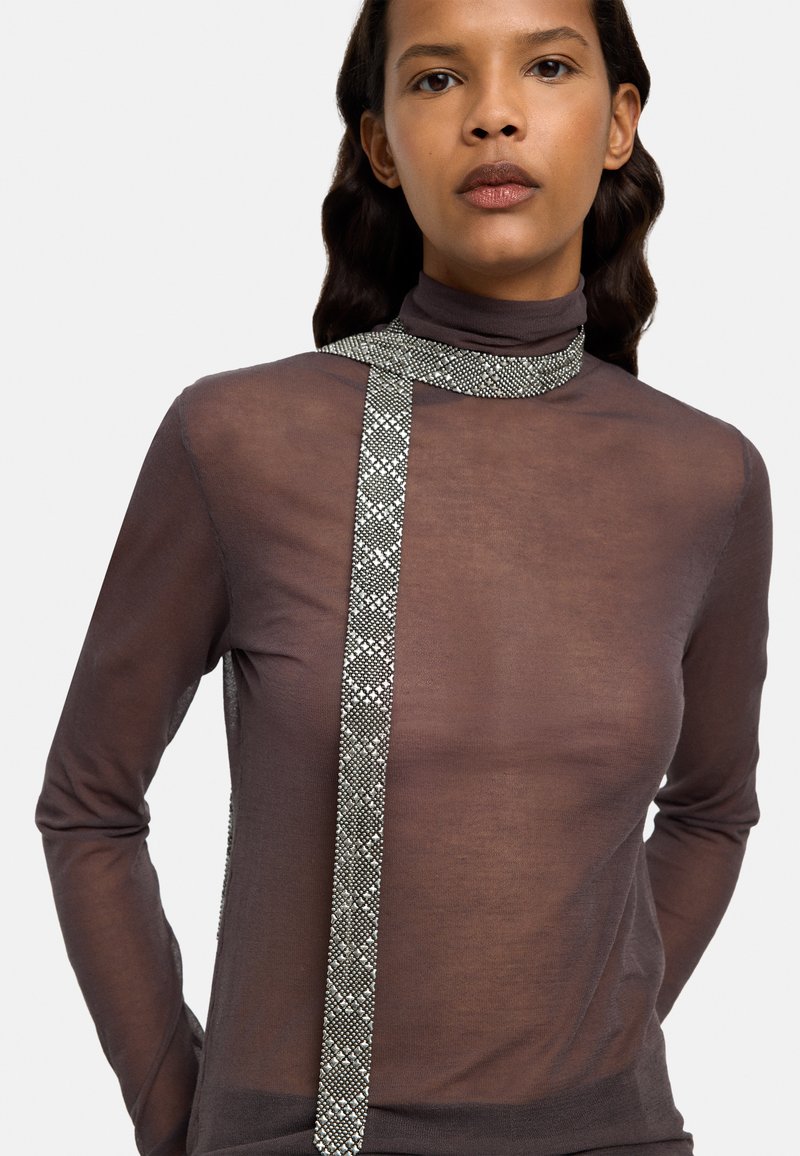 Brązowy, przezroczysty golf z ozdobnym srebrnym wykończeniem biegnącym diagonalnie wzdłuż przodu, tworzącym kontrast wizualny i fakturę.