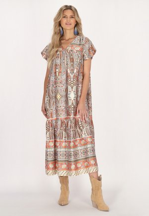 Langes, gemustertes Kleid mit V-Ausschnitt, kurzen, puffärmeligen Ärmeln, das über komplexe Designs in erdigen Tönen und einen gestuften Saum verfügt. Paar beige Cowboy-Stiefel.