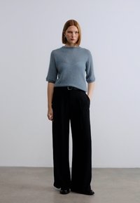 Ανοιχτό μπλε πουλόβερ με κοντά μανίκια, σε συνδυασμό με μαύρο, φαρδύ, ψηλόμεσο παντελόνι. Ομαλές υφές και μινιμαλιστικός σχεδιασμός.