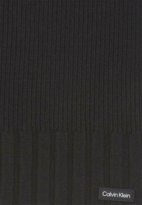 Berretto di maglia nera con texture a coste, dotato di un'etichetta tessuta con "Calvin Klein" in lettere bianche sul lato.