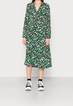 Blomstret kjole i grøn med lange ærmer, V-udskæring og lagdelt kant. Båret med sort-hvide sneakers.