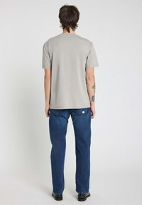 T-shirt gris à manches courtes, jeans en denim droit bleu foncé, portés avec des chaussures noires. Design simple sans motifs ou accents notables.