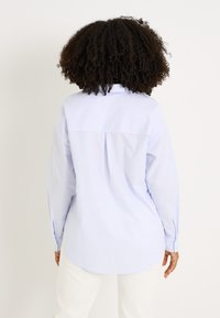 Camisa de rayas azul claro y blancas con mangas largas, puños abotonados, piqué en la espalda y dobladillo curvado. Confeccionada en suave tejido de algodón.