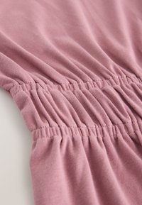 Gros plan sur un tissu rose avec des coutures élastiques froncées créant une texture plissée et un détail extensible.