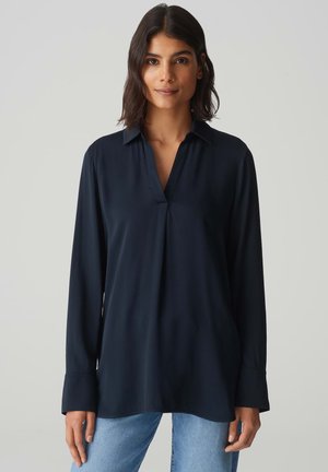 Dunkelblaue Bluse mit langen Ärmeln, Knopfleiste vorne, kragenförmigem Ausschnitt, sanftem Fall und geknöpften Manschetten, getragen über hellblauen Jeans.