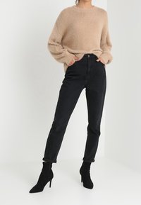 Beige wollen trui met lange mouwen gecombineerd met hoge zwarte jeans, afgemaakt met zwarte stiletto enkellaarsjes.